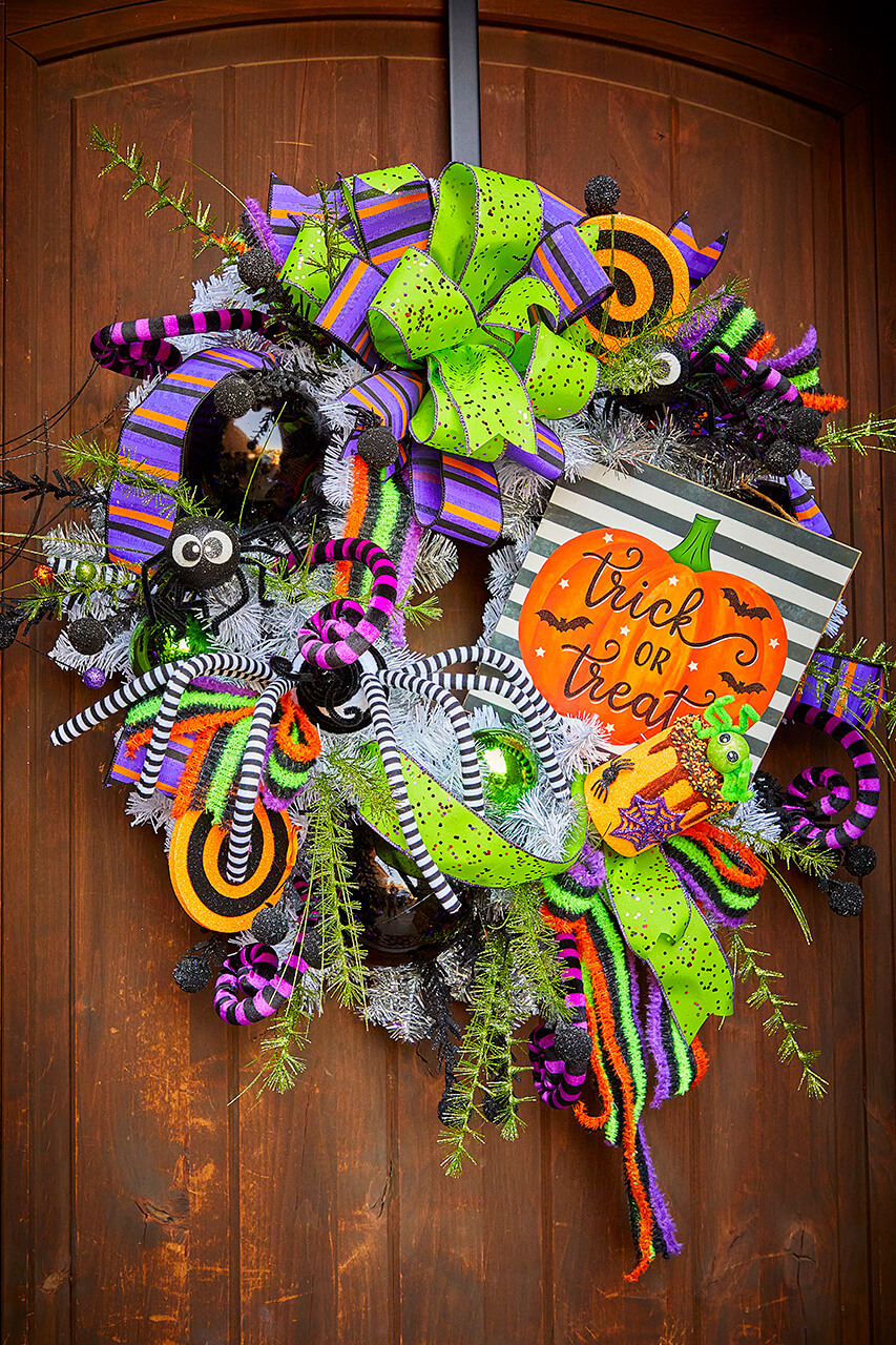 Front porch decorated with orange, purple, and lime green Halloween wreaths and garlands for outdoor Halloween decorations.